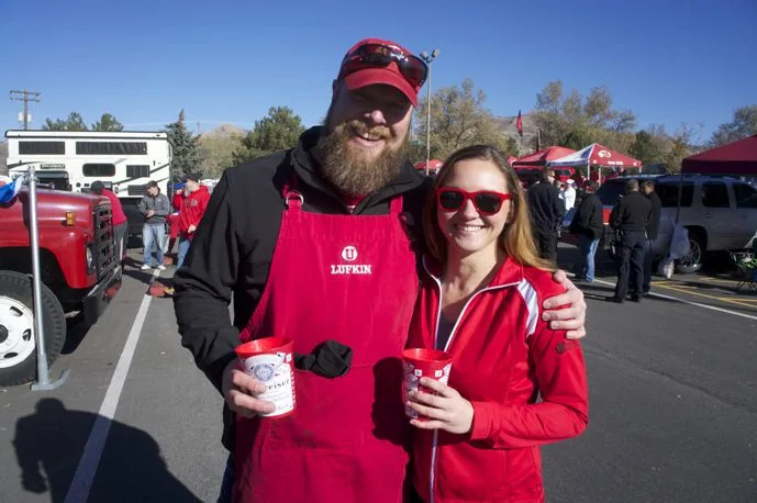Two tailgate guests in Utah gear with drinks in the lot