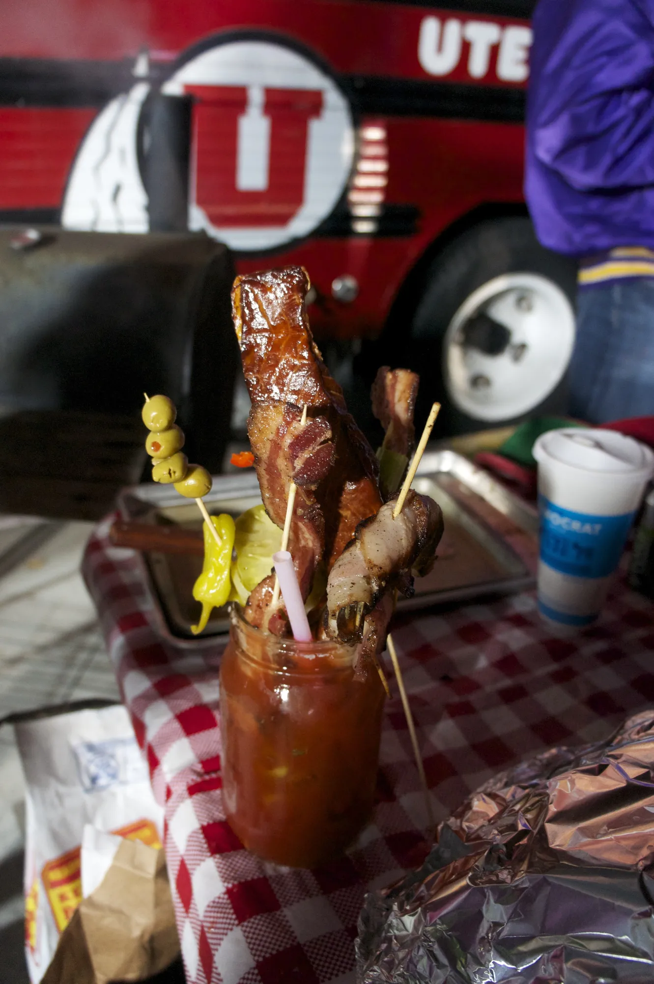 A loaded Bloody Mary with skewered snacks on a checkered tailgate table
