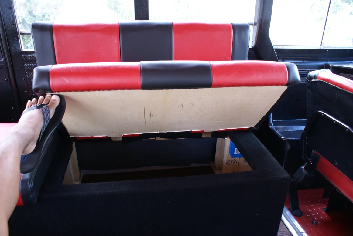 A crew member lifting a bench seat with one foot to show the storage box underneath