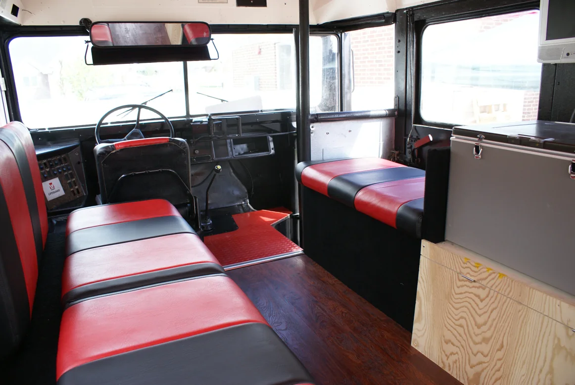 The front of the bus: benches, driver seat, a cushioned side seat and the fridge