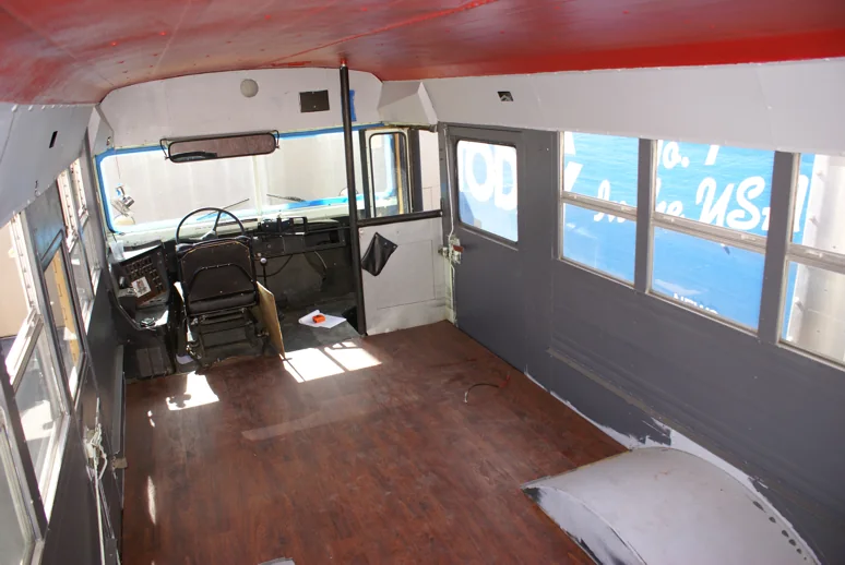 The stripped bus interior with new gray walls, red ceiling and wood-look floor