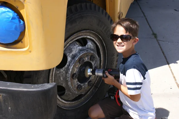 Young helpers working on the yellow bus wheels during prep