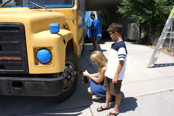 Young helpers working on the yellow bus wheels during prep