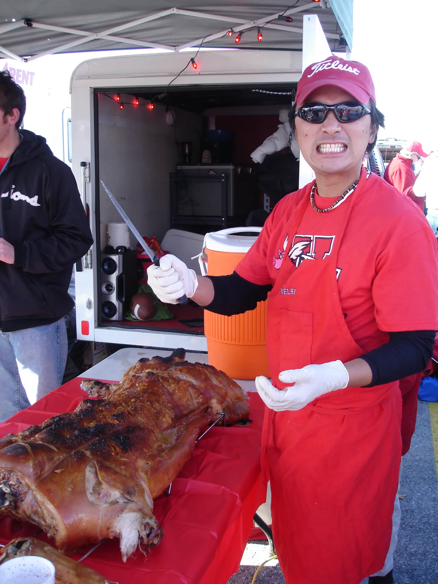 A crew member in a red apron and gloves beside a whole roasted pig