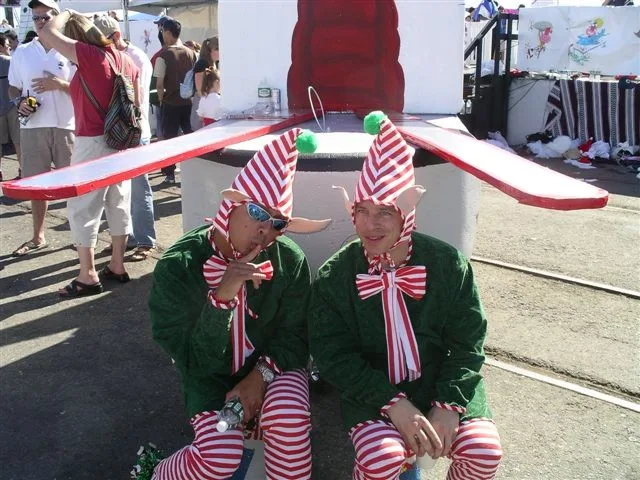Two crew members in green elf costumes and striped stockings by the flying machine