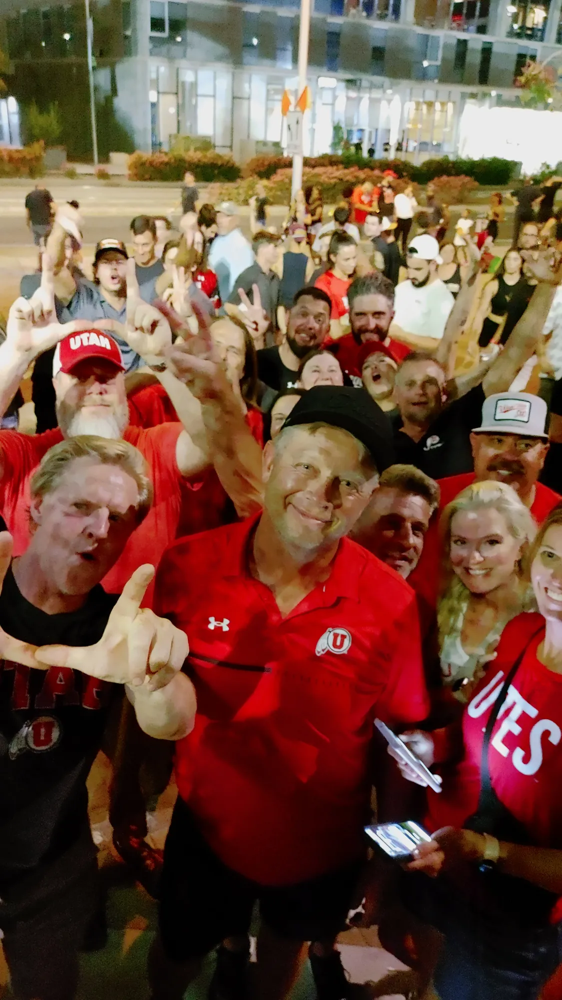 A big crowd of fans in red throwing the U sign for a selfie in the lot
