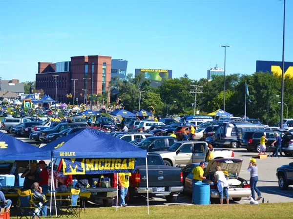 A packed Michigan football tailgate lot full of blue and maize tents, trucks and fans under a clear sky