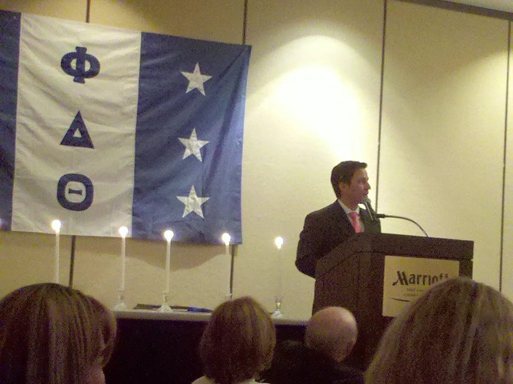 A speaker at a podium beside a Phi Delta Theta banner at a chapter event