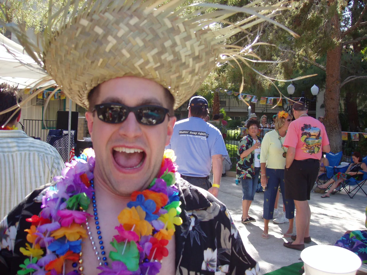 A crew member in a big straw hat, leis and sunglasses, mid-laugh