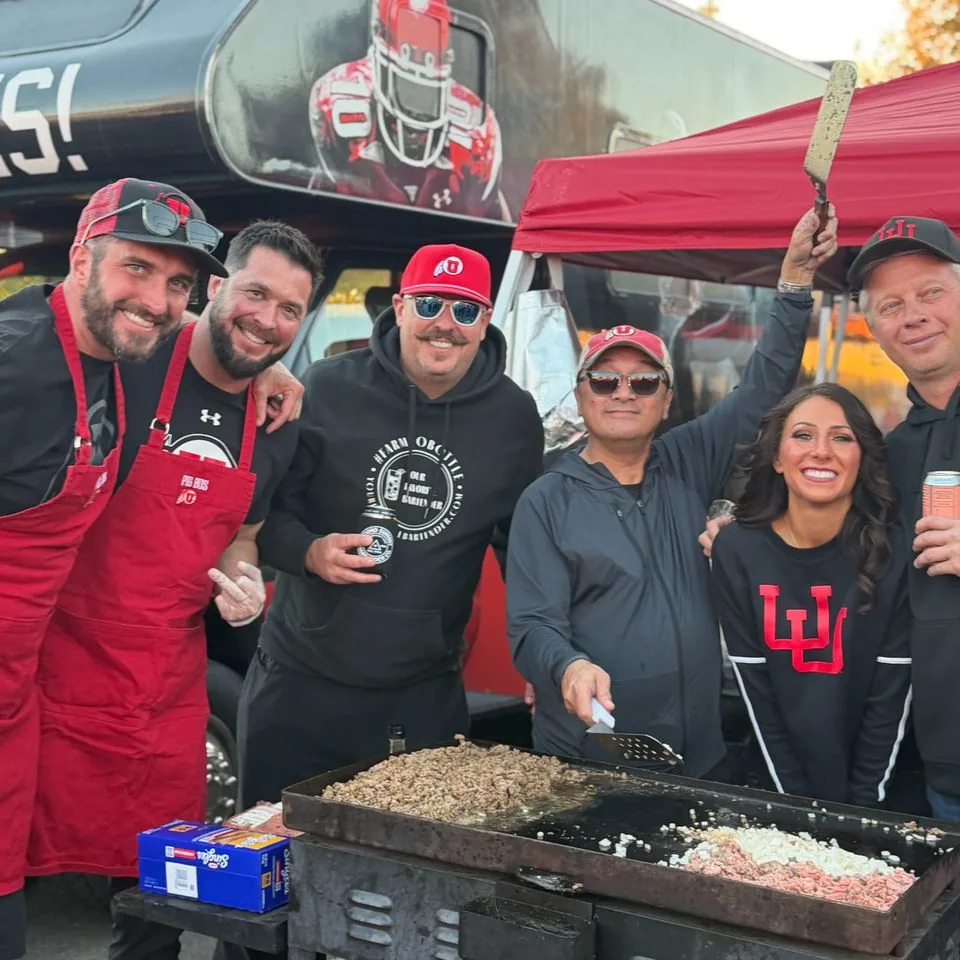 Crew members in red aprons around a flat-top griddle of sizzling meat