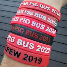 A stack of Utah Pig Bus wristbands on one arm, from Crew 2019 up to 2026