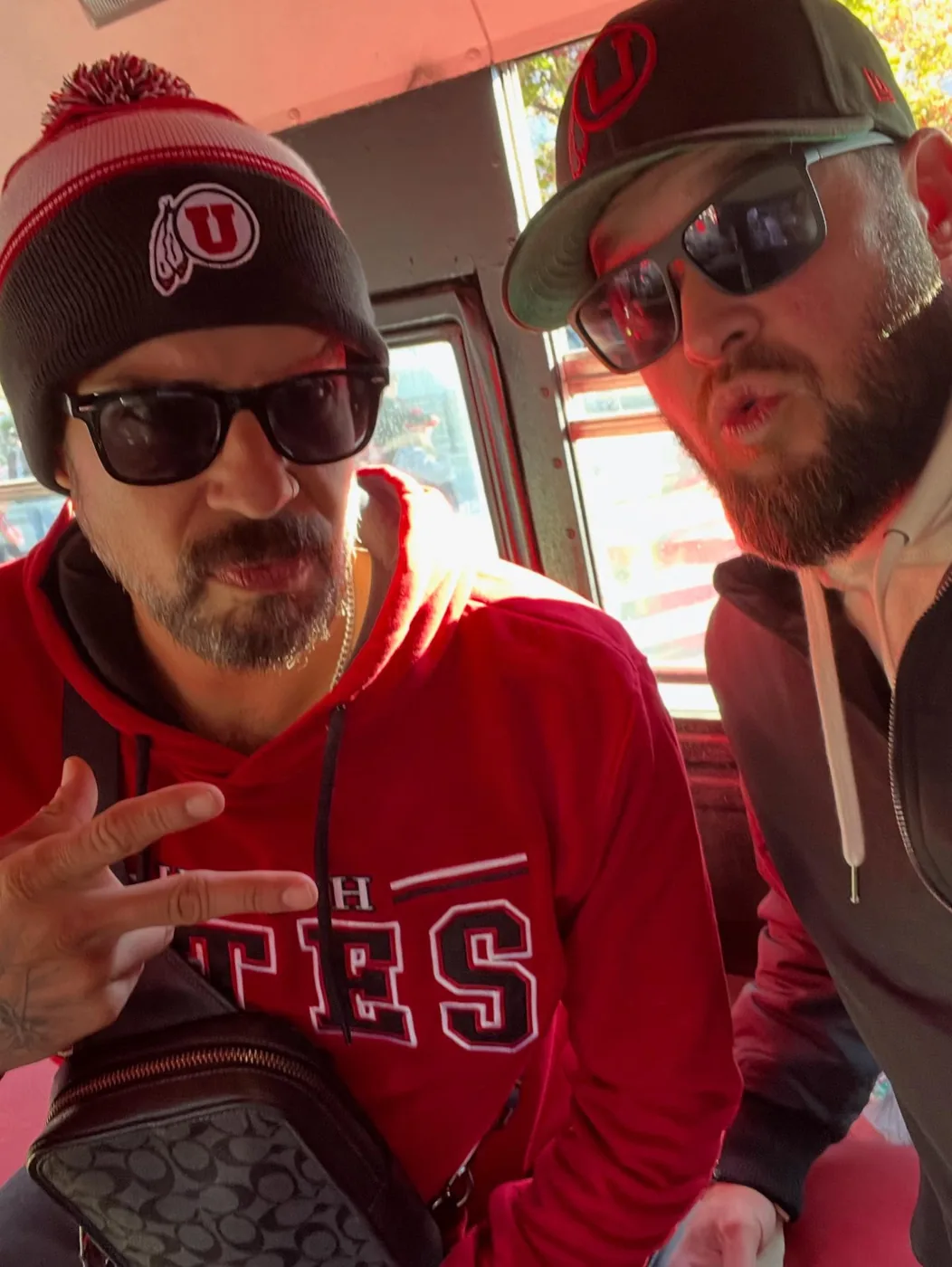 Two friends in Utah gear and sunglasses posing inside the bus