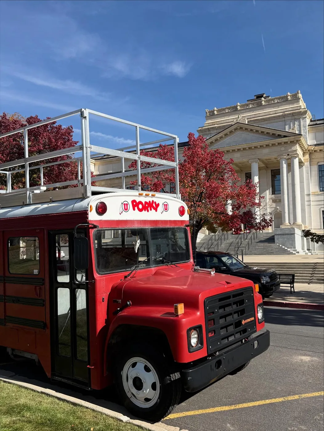 Porky parked on campus beside red autumn trees and a columned building