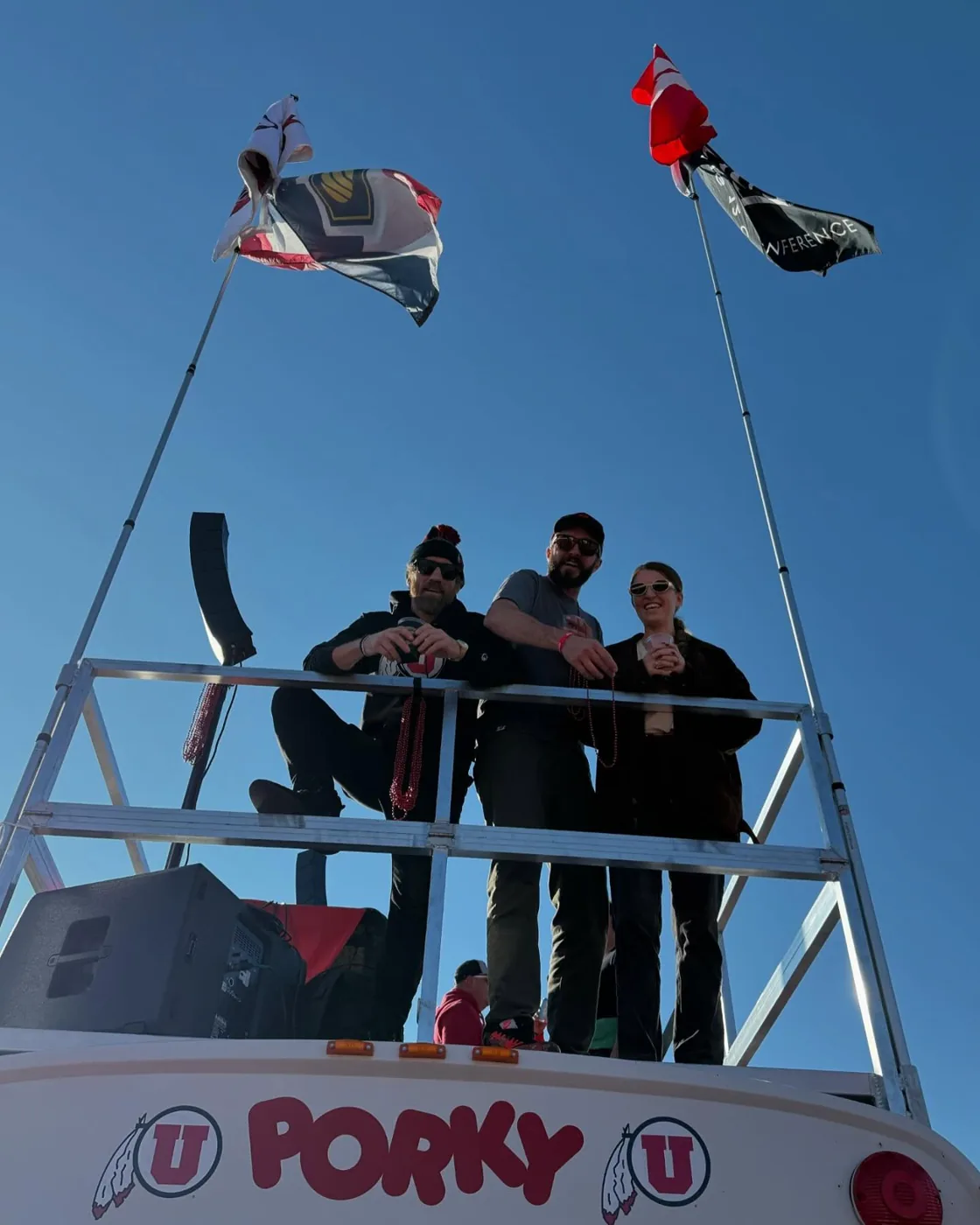 Three friends with red beads on Porky’s roof deck under the flags