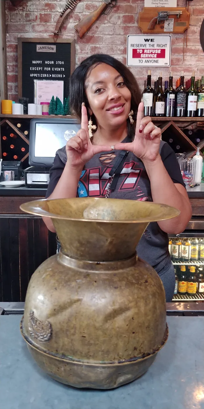 A fan throwing the U behind an old brass spittoon at a bar