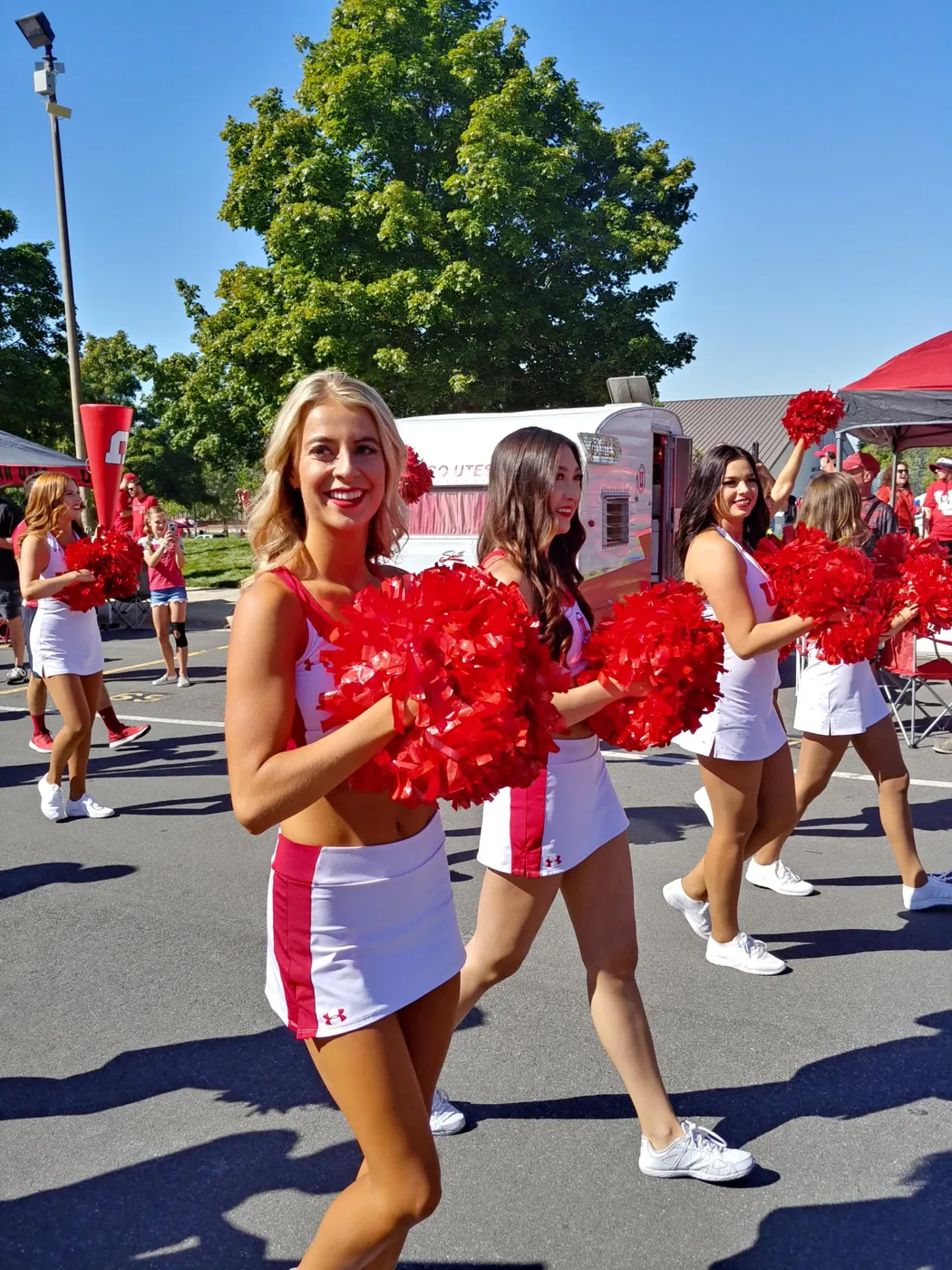 Utah cheerleaders with red pom-poms walking through the tailgate lot