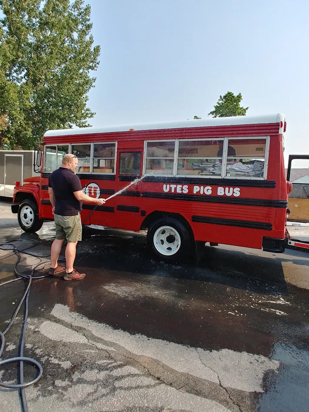 A crew member hosing down Porky, the red UTES PIG BUS with fresh white wheels