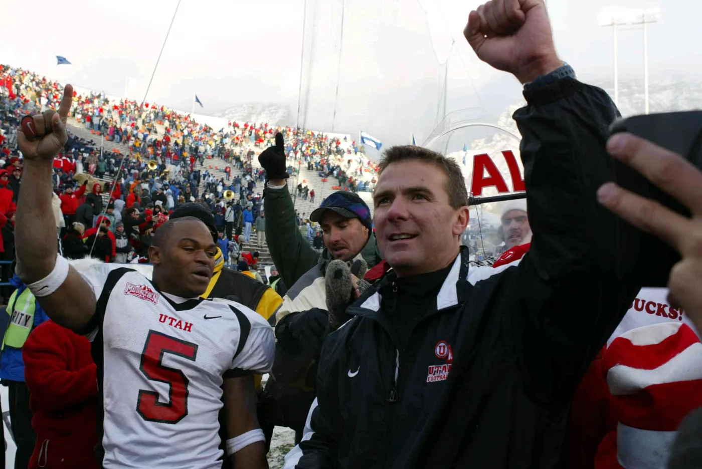 Coach Urban Meyer raising a fist with a Utah player celebrating after a snowy win