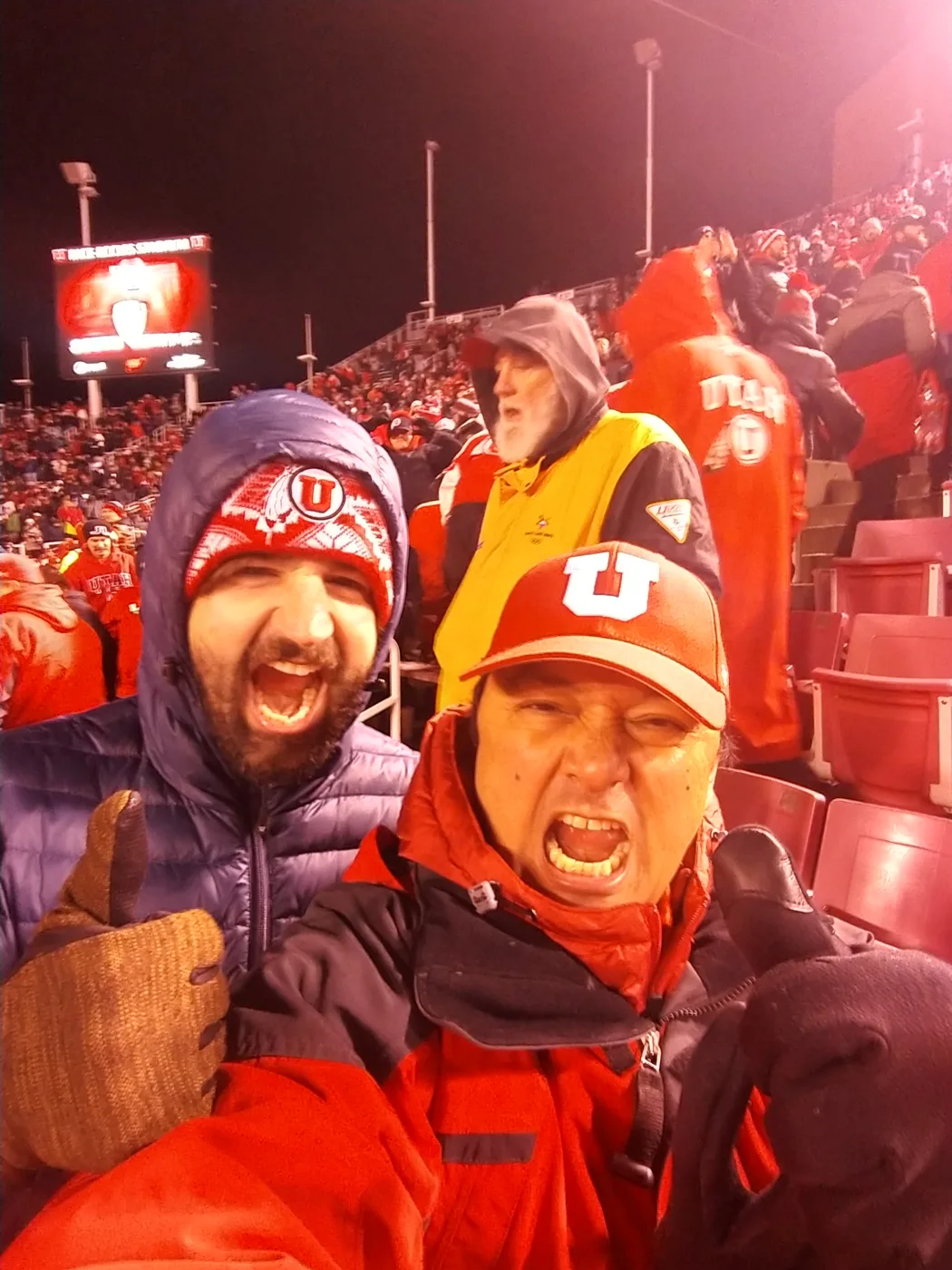 Two Utah fans shouting with excitement in the stands on a cold night at Rice-Eccles